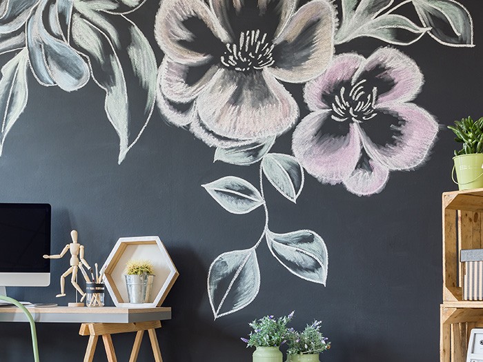 Tableau noir sur un mur présentant un motif floral coloré à la craie placé derrière un bureau et une bibliothèque.