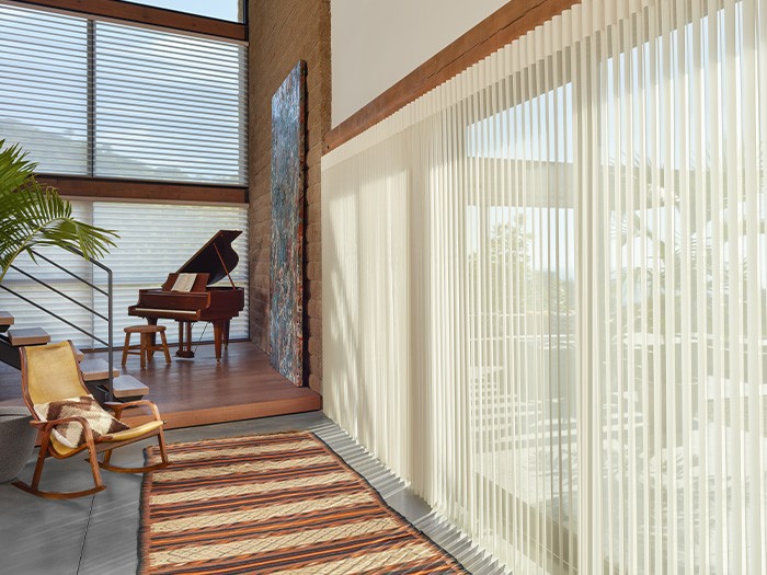 Piano and rocking chair near large windows.